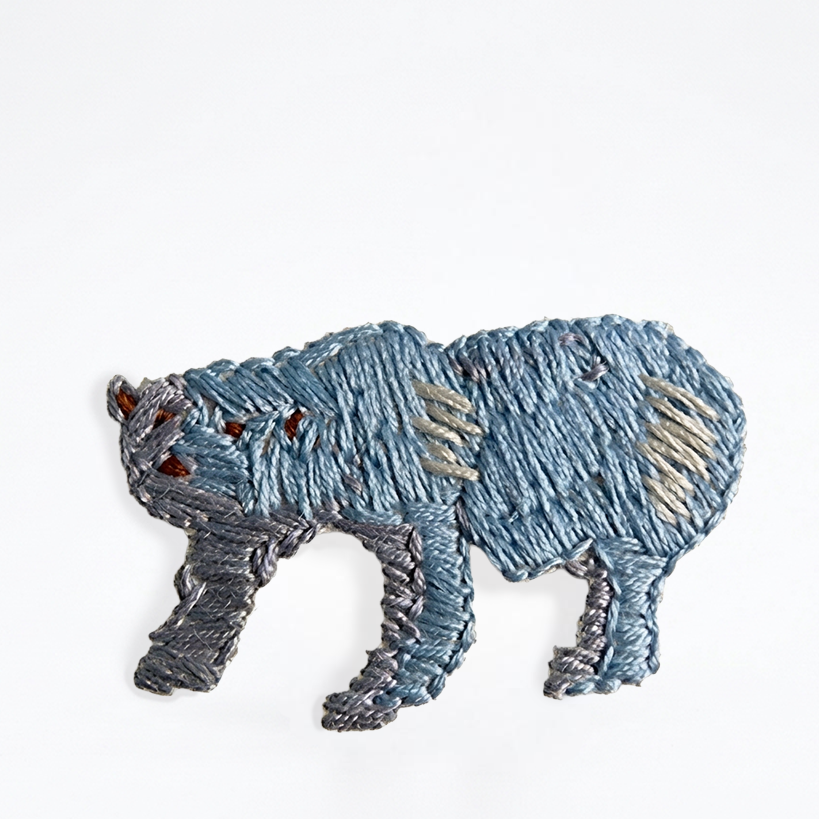 embroidered bear in blue thread, textile object with visible stitch texture on a light background