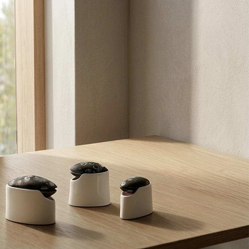 Three small containers with sliding lids made from recycled fishing floats, placed in 3D-printed holders in wood-based filament on a wooden surface.